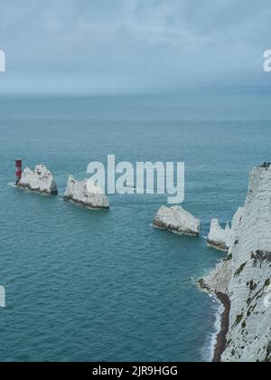 Le phare au niveau des aiguilles dans une mer acidiée et derrière des affleurements déchiquetés, ressemblant à des dents qui s'étendent de la falaise, qui montrent clairement pourquoi la balise est nécessaire Banque D'Images