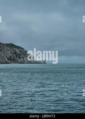 Le phare au niveau des aiguilles derrière des affleurements dentelés, qui expliquent clairement pourquoi le phare est nécessaire, dans une mer à ciel ouvert sous un ciel couvert. Banque D'Images