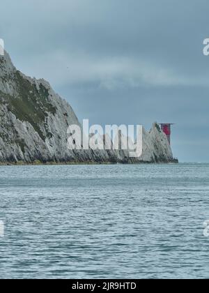 Le phare au niveau des aiguilles derrière des affleurements dentelés, qui expliquent clairement pourquoi le phare est nécessaire, dans une mer à ciel ouvert sous un ciel couvert. Banque D'Images