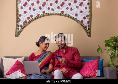 Portrait de heureux jeune couple shopping en ligne par ordinateur portable en utilisant la carte de crédit à la maison Banque D'Images