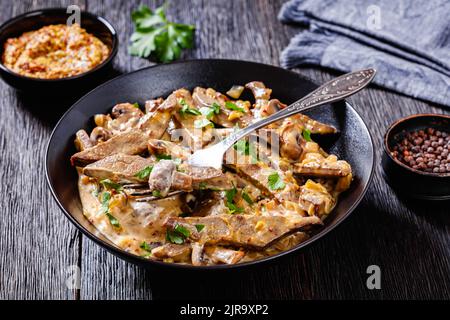 foie de bœuf, moutarde à la wholegrain, oignon et champignons, dans un bol noir sur une table en bois sombre, vue horizontale depuis le dessus Banque D'Images