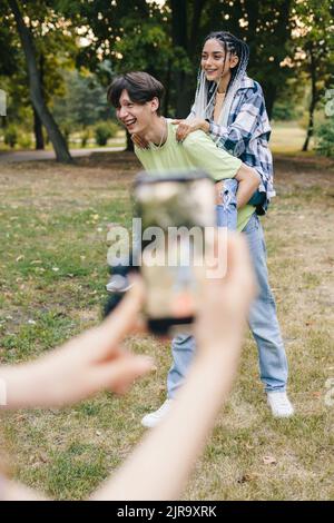 Un garçon souriant et une fille dansant devant l'iPhone gardé par leur petite amie enregistrant la vidéo. Smartphone avec application populaire. Banque D'Images