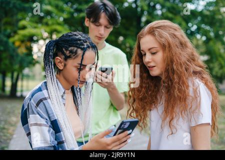 Trois jeunes blancs modernes heureux d'obtenir beaucoup de réactions positives sur leurs messages Internet. Création d'une vidéo pour Internet à l'aide d'un smartphone Banque D'Images