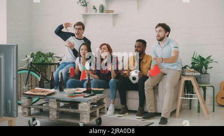 Groupe multiethnique d'amis fans de sport avec drapeaux portugais regardant le championnat de football à la télévision ensemble à la maison à l'intérieur et encourageant l'équipe préférée Banque D'Images