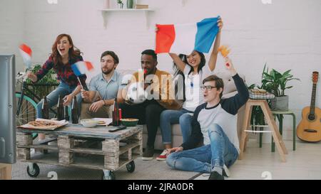 Groupe multiethnique d'amis fans de sport avec drapeaux français regardant le championnat de football à la télévision ensemble à la maison à l'intérieur et encourageant l'équipe préférée Banque D'Images
