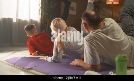 Grand-parents et petit-fils s'entraîner à la maison et faire un entraînement musculaire sur une jambe sur un tapis de fitness ensemble Banque D'Images