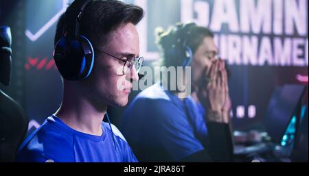 Esportsman joue avec des lunettes en mettant des écouteurs et en butant des poings avec des coéquipiers au début du tournoi de jeu professionnel Banque D'Images