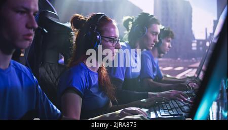 Concentration de jeunes femmes esportsman joueur dans le jeu de lunettes de tir sur l'ordinateur tout en étant assis parmi les coéquipiers pendant le tournoi de jeu Banque D'Images