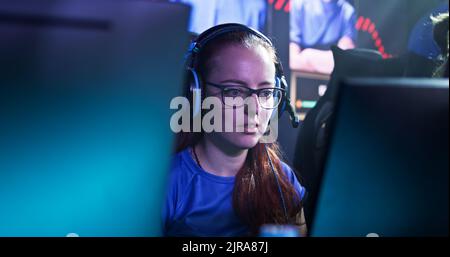 Femme joueur d'Esportsman dans des lunettes et des écouteurs communiquant avec ses coéquipiers et exprimant sa déception lors de jeux vidéo sur ordinateur pendant la compétition esports Banque D'Images