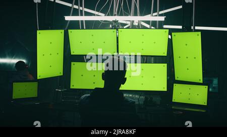 Zoom avant visualiser un homme méconnaissable qui écrit du code malveillant sur des ordinateurs tout en étant assis contre des moniteurs d'ordinateur avec des écrans chromakey dans la pièce sombre de la base de hacker Banque D'Images