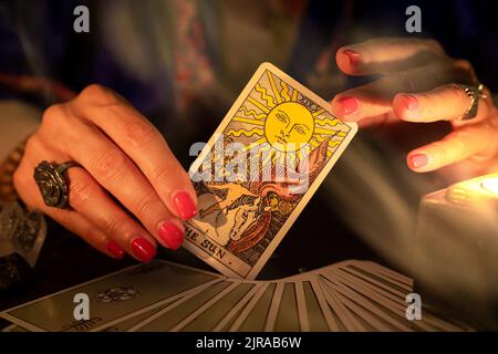 Les mains des filles de la caissière montrant la carte du Soleil, symbole de positivité et d'optimisme, pendant une lecture. Gros plan avec bougie et fumée Banque D'Images