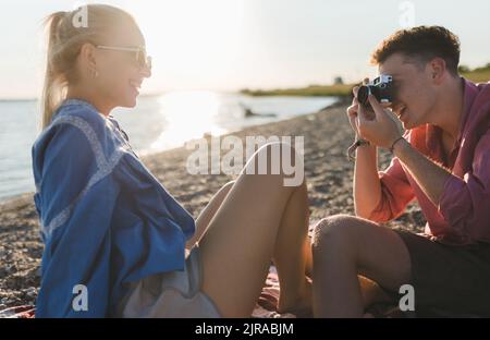 Jeune garçon prenant la photo de sa belle petite amie à la plage pendant le coucher du soleil. Banque D'Images