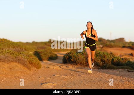 Coureur femme en train de courir vers l'appareil photo au coucher du soleil dans la montagne Banque D'Images