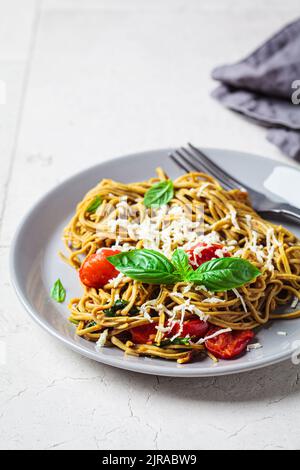 Pâtes végétaliennes vertes aux haricots avec tomates, basilic et noix dans une assiette grise. Concept alimentaire sain à base de plantes. Banque D'Images