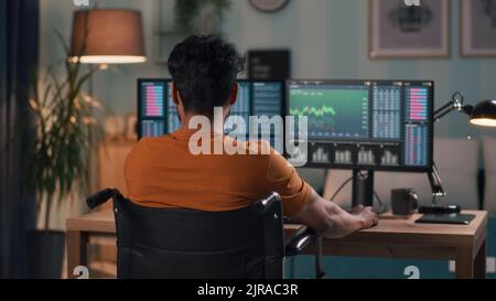 Anonyme homme en t shirt orange analyse des graphiques sur des moniteurs d'ordinateur tout en négociant sur le marché boursier en ligne à la maison Banque D'Images