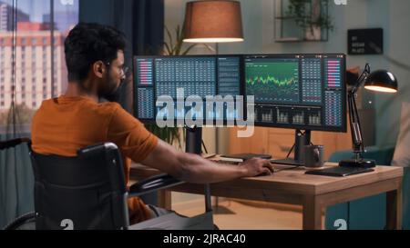 Anonyme homme en t shirt orange analyse des graphiques sur des moniteurs d'ordinateur tout en négociant sur le marché boursier en ligne à la maison Banque D'Images