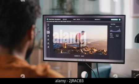 Vue arrière de l'homme anonyme intégrant le graphique 3D dans la vidéo avec la personne réelle tout en étant assis à la table et en utilisant l'ordinateur dans le bureau à domicile Banque D'Images