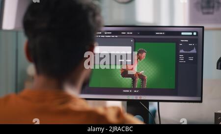 Vue arrière de l'homme anonyme intégrant le graphique 3D dans la vidéo avec la personne réelle tout en étant assis à la table et en utilisant l'ordinateur dans le bureau à domicile Banque D'Images