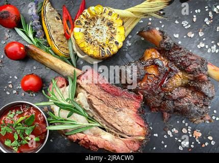 Côtes de bœuf grillées sur un tableau noir en ardoise avec maïs et sauce. Vue de dessus, gros plan Banque D'Images