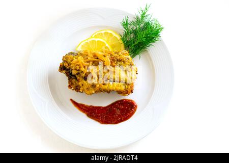 Poisson frappé sur une plaque de céramique blanche avec citron, sauce rouge et herbes sur un fond blanc isolé. Ingrédients : morue, pâte, aneth. Copier l'espace pour votre menu . Banque D'Images