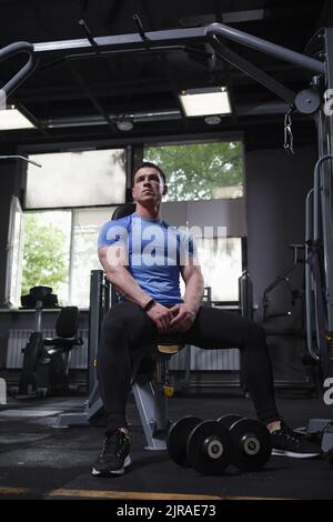 Plan vertical en longueur d'un bodybuilder se reposant après l'exercice avec des haltères à la salle de gym Banque D'Images