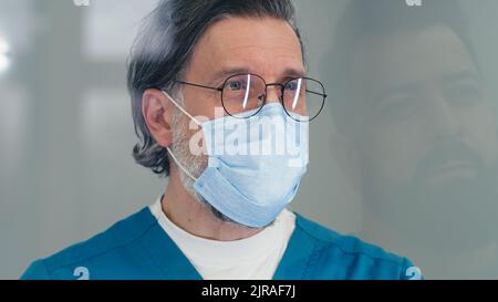 Un médecin mature en masque pose des questions au médecin tout en travaillant à l'accueil de l'hôpital pendant une pandémie Banque D'Images