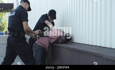 Homme et femme en uniforme de police attachant les menottes et dirigeant l'Africain américain coupable loin dans la rue de la ville Banque D'Images