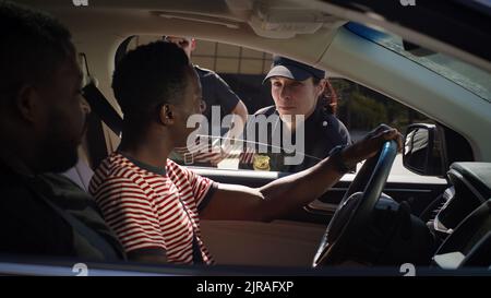 Des hommes afro-américains se gesticulent et discutent de la présence d'une femme sérieuse en uniforme de police lorsqu'elle est assise en voiture après vérification des documents Banque D'Images