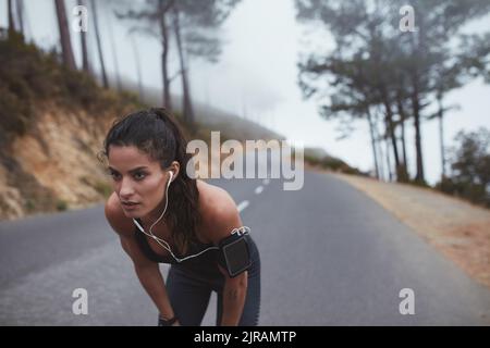 Une femme qui fait une pause pour s'adonner à l'activité en extérieur. Jeune femme sportive ayant une séance d'entraînement le matin le long d'une route de campagne brumeuse. Banque D'Images