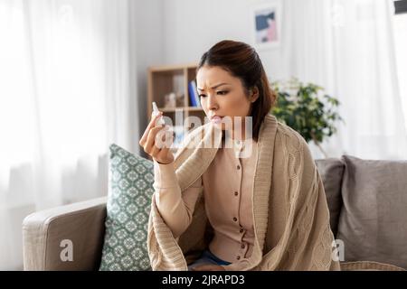 femme asiatique malade avec un traitement nasal par pulvérisation à la maison Banque D'Images