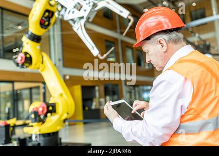 Un travailleur qualifié contrôlant le bras du robot avec une tablette numérique Banque D'Images