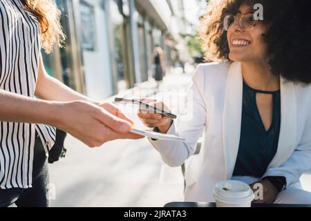 Jeune femme d'affaires qui paie par téléphone intelligent au café Sidewalk Banque D'Images