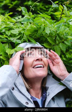 Femme souriante portant un coupe-vent devant les feuilles Banque D'Images