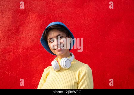 Femme souriante avec un casque et un chapeau en forme de seau devant le mur rouge Banque D'Images