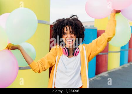 Bonne femme tenant des ballons colorés devant des tuyaux Banque D'Images