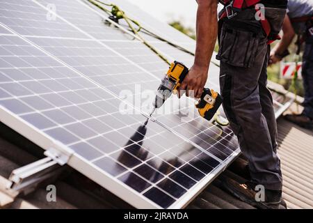 Électricien utilisant un outil électrique pour installer le panneau solaire sur le toit Banque D'Images