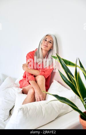 Femme d'âge mûr assise sur un canapé à la maison Banque D'Images