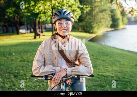 Femme souriante avec casque assis sur un vélo au parc Banque D'Images