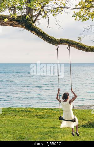 Femme assise sur balançoire au bord de la mer Banque D'Images