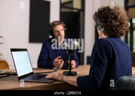 Présentateur portant un casque d'écoute pour interroger le client dans un studio d'enregistrement Banque D'Images