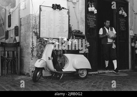 Une photo en niveaux de gris d'un scooter italien Vespa garée devant un café à Rome Banque D'Images