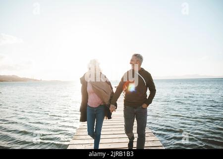 Couple d'âge mûr heureux tenant les mains marchant sur la jetée Banque D'Images