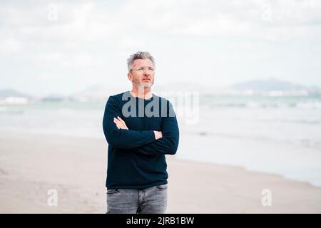 Homme mûr et réfléchi avec les bras croisés debout à la plage Banque D'Images