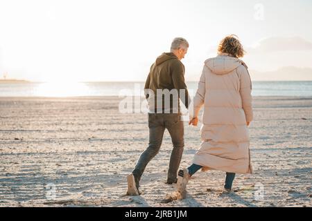 Couple d'âge mûr tenant les mains marchant à la plage par beau temps Banque D'Images