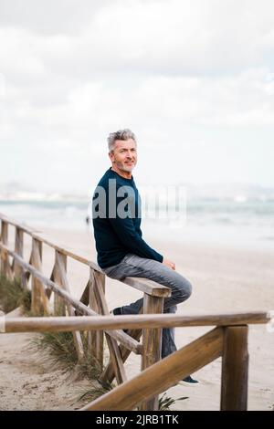 Heureux homme mûr assis sur une rampe à la plage Banque D'Images