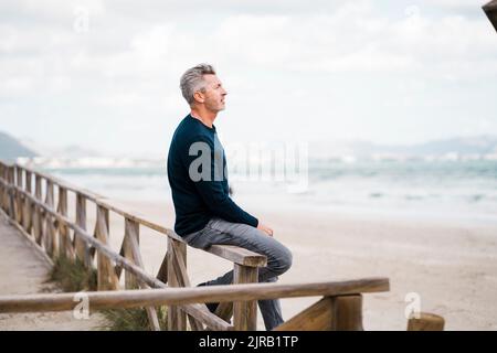 Homme mûr et réfléchi assis sur une rampe à la plage Banque D'Images