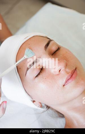 Gros plan esthéticienne médecin fabrication de main anti-âge procédure appliquer l'acide de peeling, jeune femme attrayante client à la clinique de beauté. Thérapie de soins de santé Banque D'Images