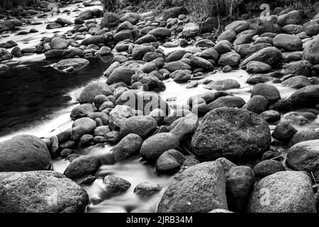 Longue exposition d'une rivière à écoulement rapide entre des blocs de basalte arrondis dans les montagnes du Drakensberg en Afrique du Sud, en noir et blanc. Banque D'Images