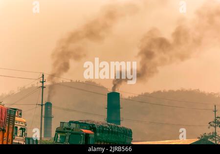 Fumée sombre à la suite de la combustion du charbon dans des fours, qui s'échappe de cheminées dans une usine de ciment à Byrnihat, Meghalaya, en Inde. Banque D'Images