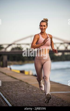 Jeune femme active qui fait du jogging sur la promenade au coucher du soleil Banque D'Images